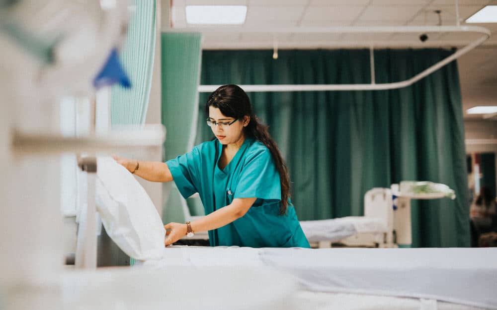 Nurse straightening patient bed in hospital room